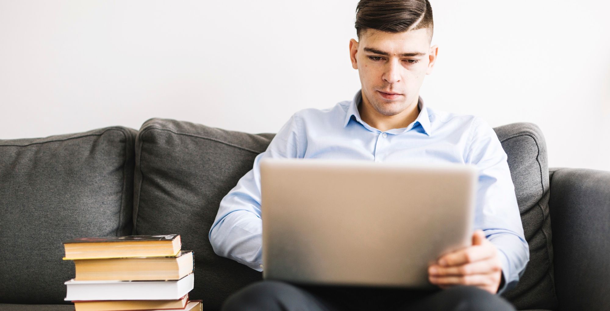 estudante universitário sentado em um sofá com seu computador e livros