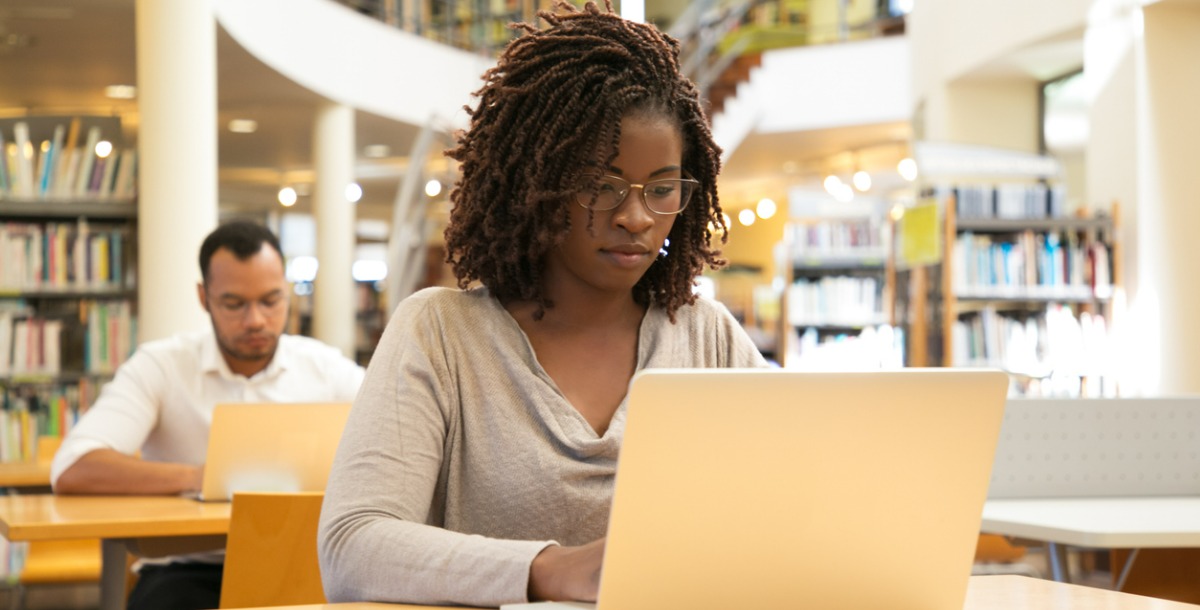 estudante do sexo feminino que utiliza o seu computador a partir da secretária da biblioteca