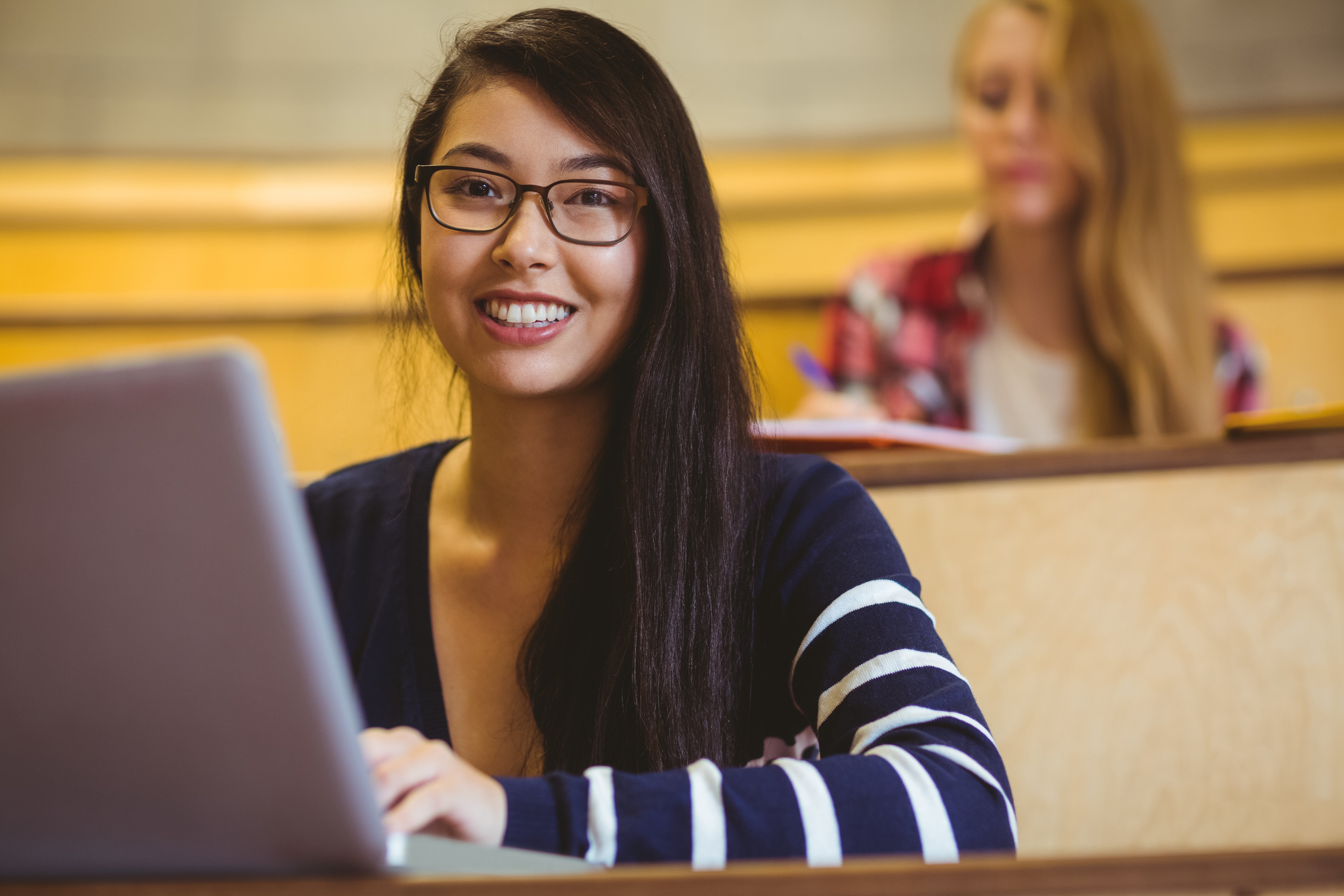 Mulher sentada com um laptop aberto e sorrindo para a câmera